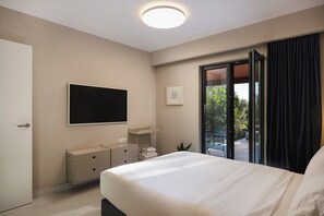 A bedroom with a bed, a flat-screen TV, a dresser, a small table, and a sliding glass door leading to an outdoor area.