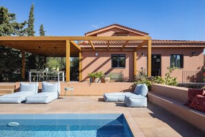 A poolside area with a covered seating area and a building with a tiled roof. - Villa Elli - A magical garden retreat with private pools and curated spaces (Rethymno)