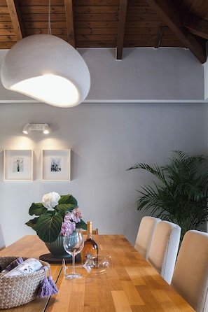 A dining area with a wooden table, chairs, a hanging light fixture, framed pictures on the wall, and a potted plant.