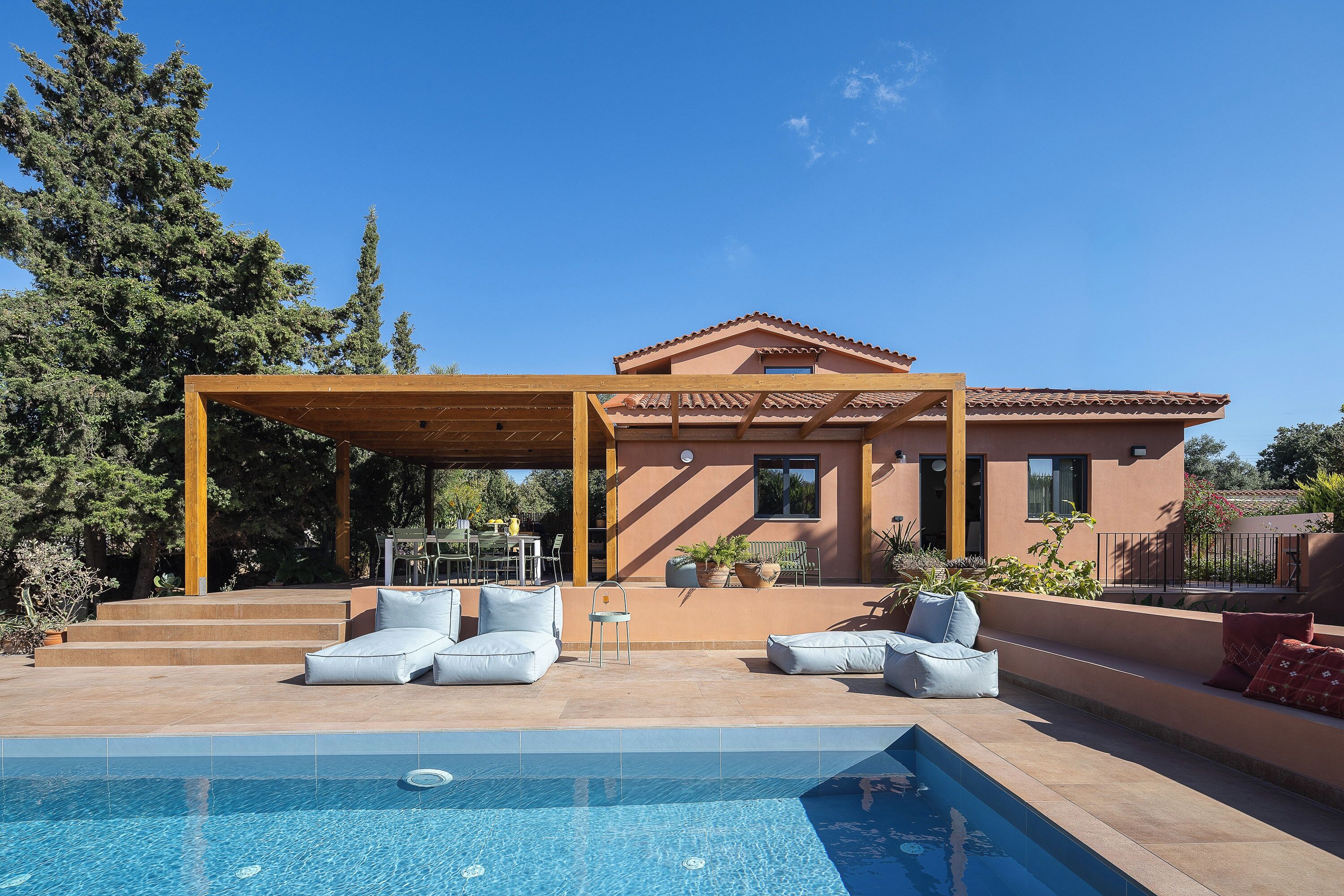 Un espace aménagé au bord de la piscine, avec un patio couvert, du mobilier d’extérieur et une piscine à l’eau d’un bleu limpide.