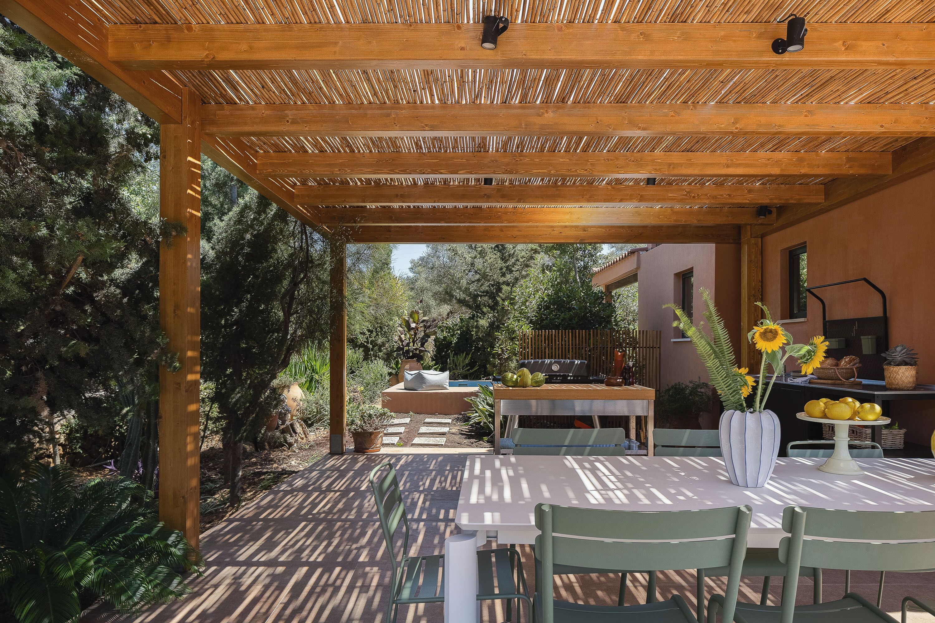 Une terrasse extérieure agrémentée d’une pergola en bois, d’une table avec des chaises, ainsi que de diverses plantes et de fruits.