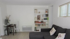 Una sala de estar con un sofá gris oscuro, una estantería blanca y un pequeño escritorio con una computadora.