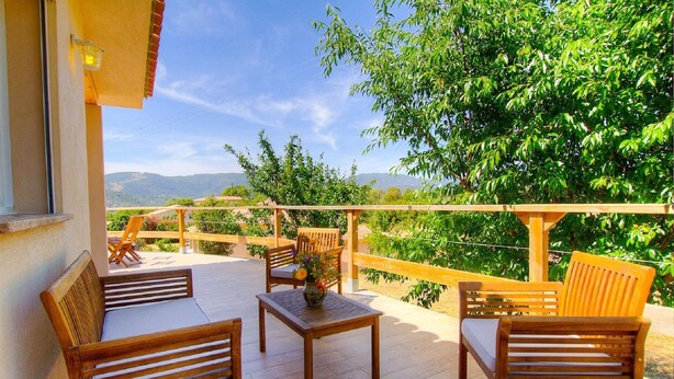A wooden deck with outdoor furniture, a wooden railing, and a view of green trees and distant hills. - Splendid villa 5 minutes from the sea (Sollacaro)