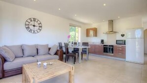A modern living room with a sofa, a wooden coffee table, and a dining area with chairs and a table. A kitchen with cabinets, a stove, and a refrigerator is visible in the background. - Splendid villa 5 minutes from the sea (Sollacaro)