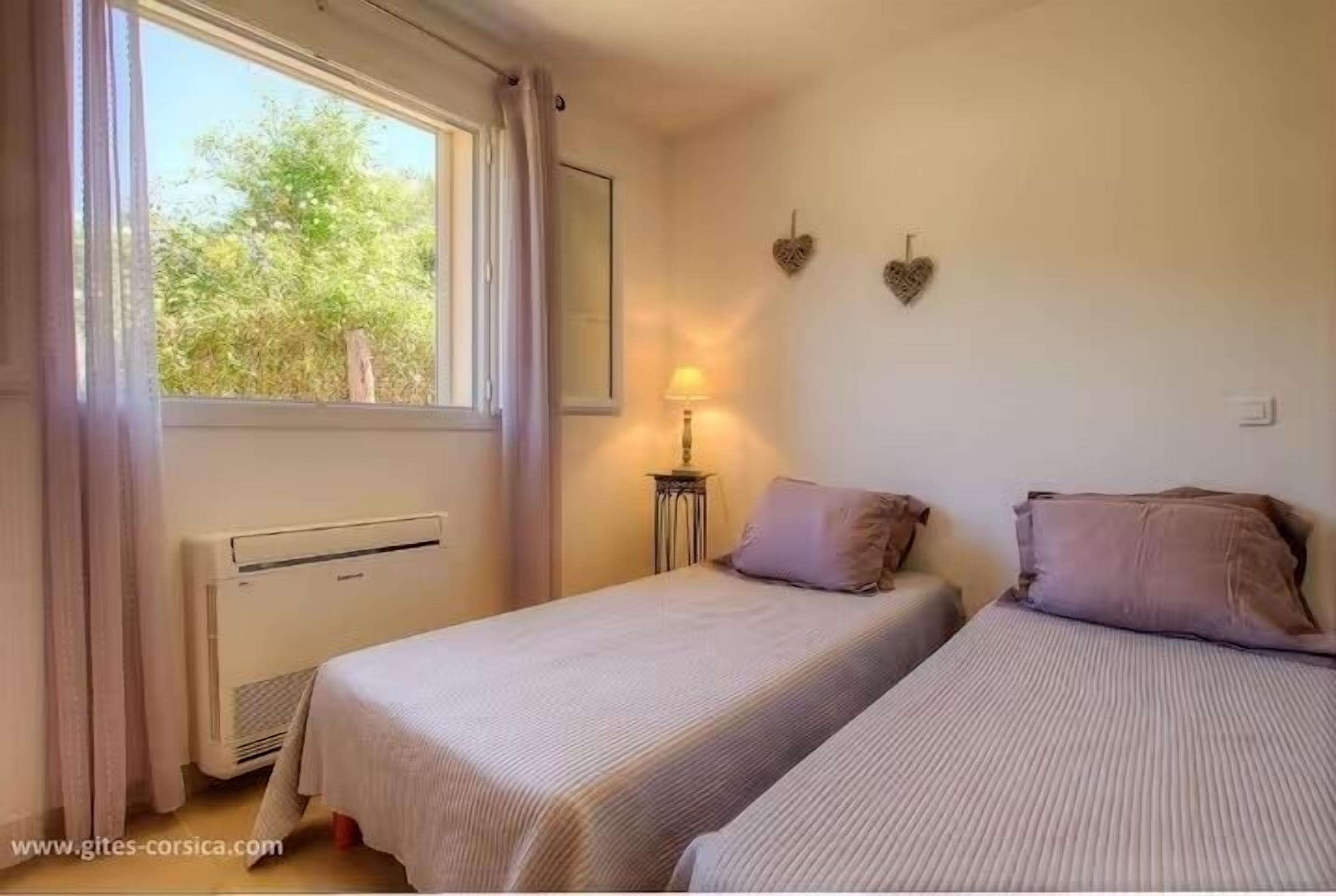 Een slaapkamer met twee bedden, een raam met gordijnen, een bedlampje en een wandradiator.