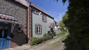 Un étroit sentier de gravier mène à une maison traditionnelle en pierre et en briques, dont la porte est bleue.