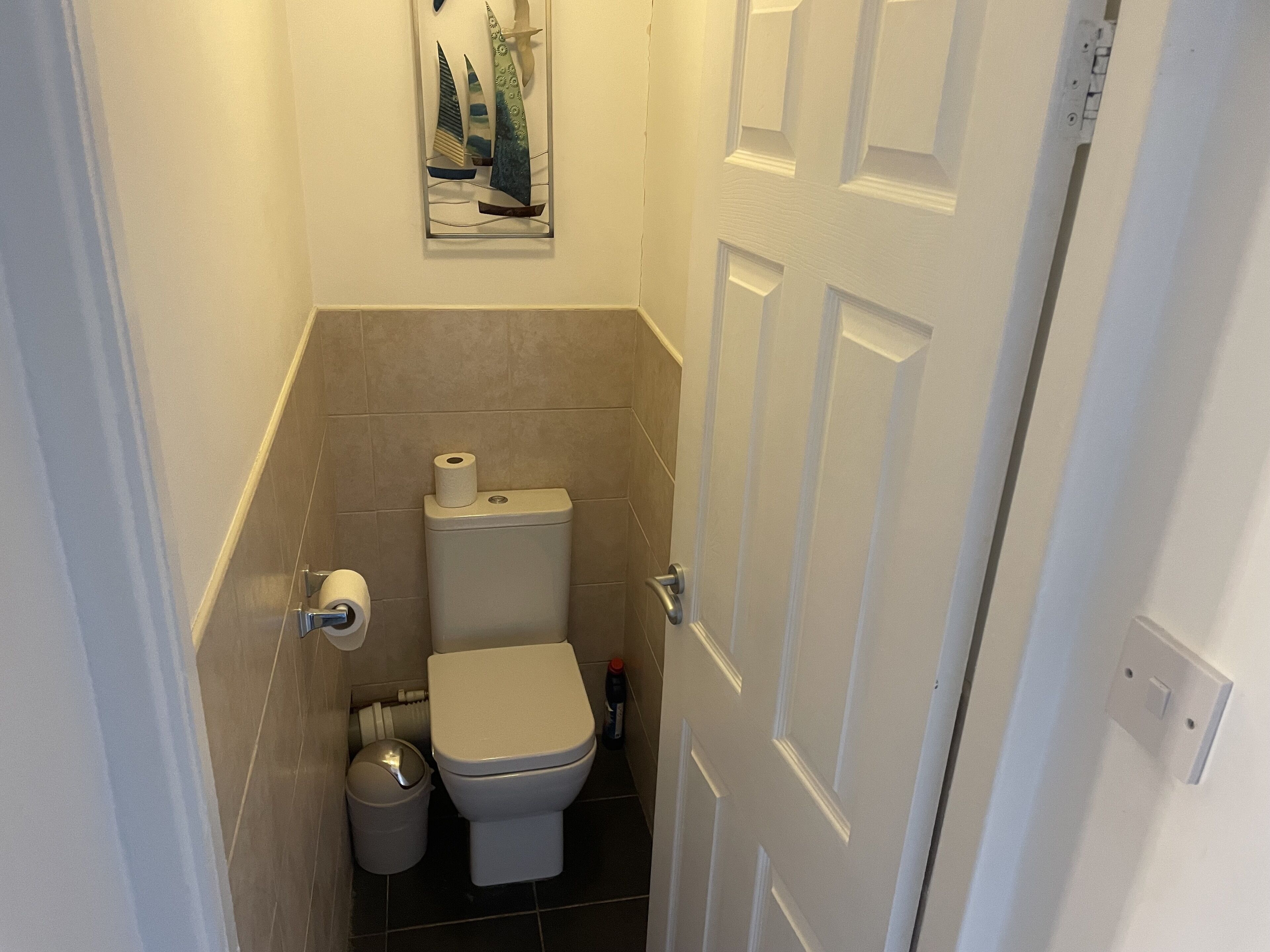 A small, compact bathroom with a toilet, a trash bin, and a toilet paper holder.