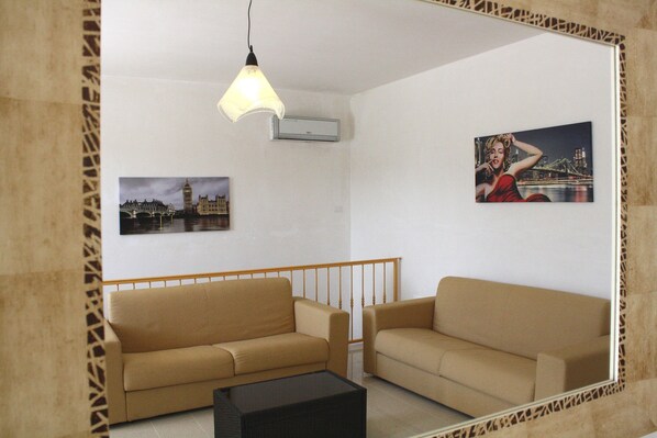 A living room with two beige sofas, a black coffee table, a hanging light fixture, and two wall-mounted pictures.