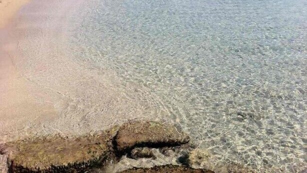 Ein Strand mit klarem, flachen Wasser, einem Sandufer und einigen Personen.
