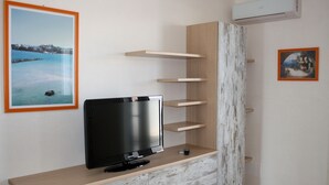 Ein modernes Wohnzimmer mit Fernseher auf einer Holzkonsole, eingebauten Regalen und einem gerahmten Bild mit Meeresblick.