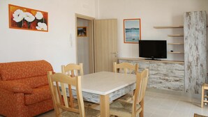Ein Essbereich mit Holztisch und Stühlen, einer Couch, einem Fernseher und einer Holzkommode.