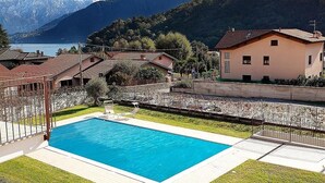 Una piscina con vistas a montañas y un lago, rodeada de casas y una valla.