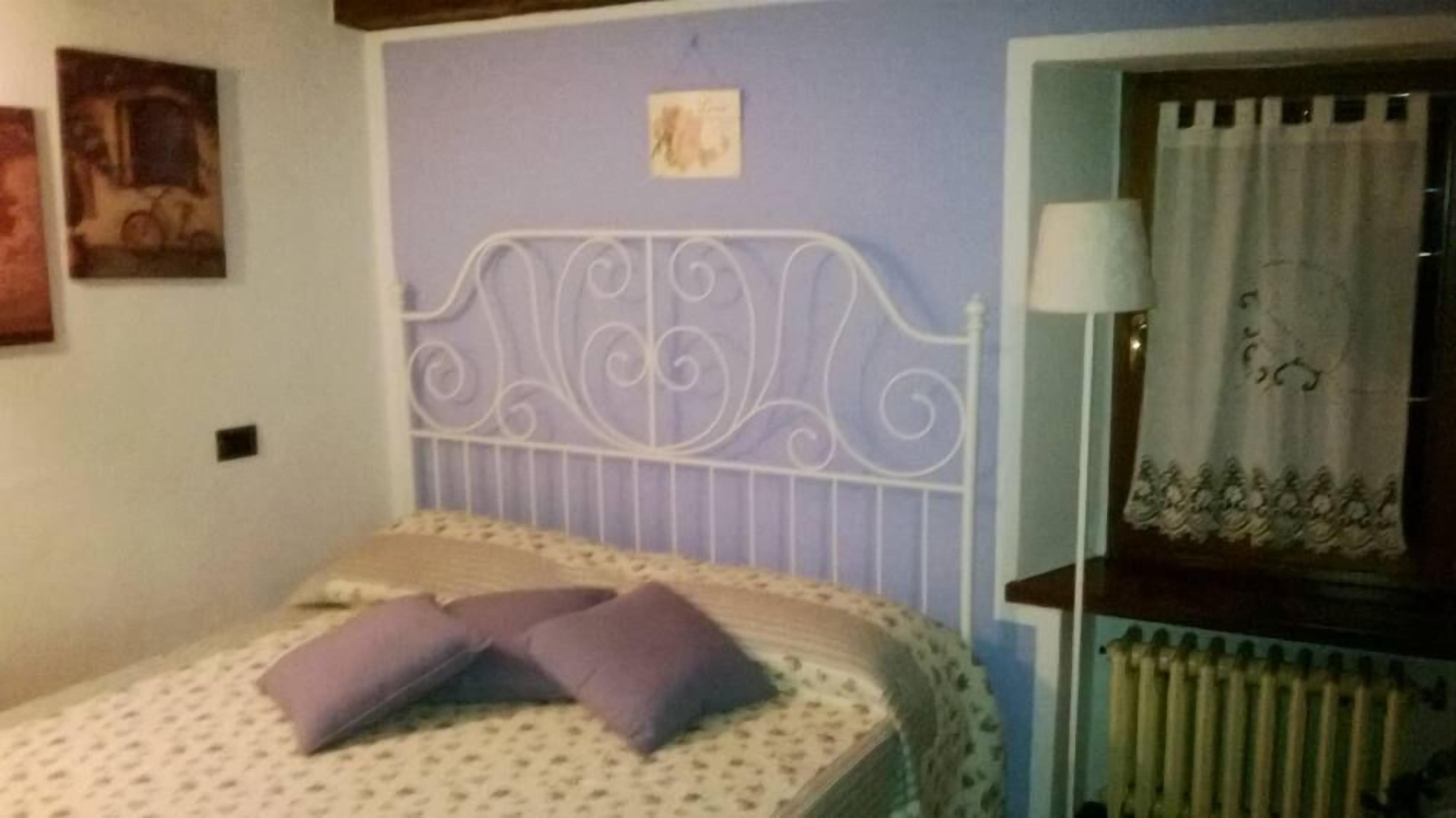 A bedroom with a bed, pillows, a radiator, a nightstand, and a wall with a picture.