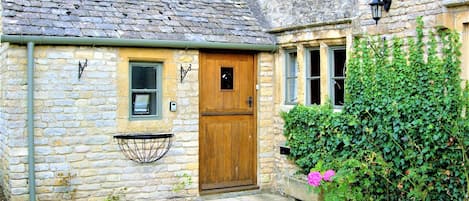 Una cabaña de piedra con puerta de madera, una ventana pequeña y una lámpara.