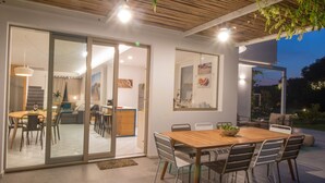 An open-plan living area with a dining table, chairs, and a kitchen visible through glass doors. - TD Villa Ponente Luxury Villa with Sea View Pool (Capitolo)