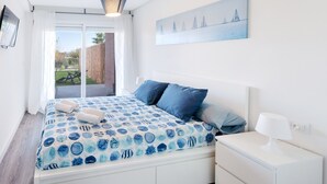 Ein Schlafzimmer mit einem Bett, einem Nachttisch, einem Gemälde und Blick ins Freie.