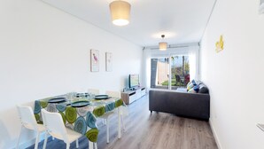 Ein moderner Essbereich mit einem Tisch für vier Personen, weißen Stühlen und einem grauen Sofa im Hintergrund.