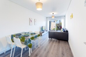 A modern dining area with a table set for four, white chairs, and a grey sofa in the background.