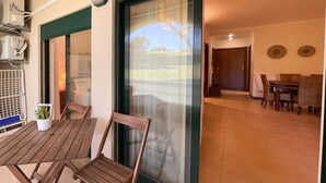 Um pátio com móveis de madeira, um vaso de planta e uma porta de vidro deslizante que dá para uma área de refeições interna com mesa e cadeiras.