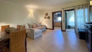 Sala de estar com sofá, mesa de jantar com cadeiras de vime, cozinha com fogão e porta de vidro deslizante para uma varanda.