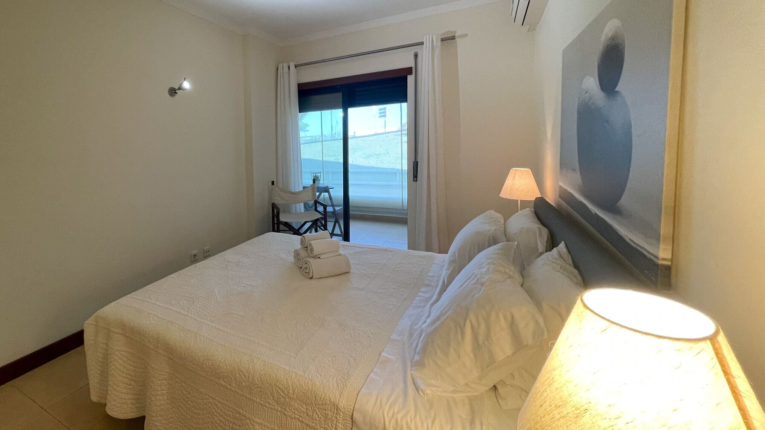 Habitación de hotel con cama, lámpara, cuadro y vistas al exterior.