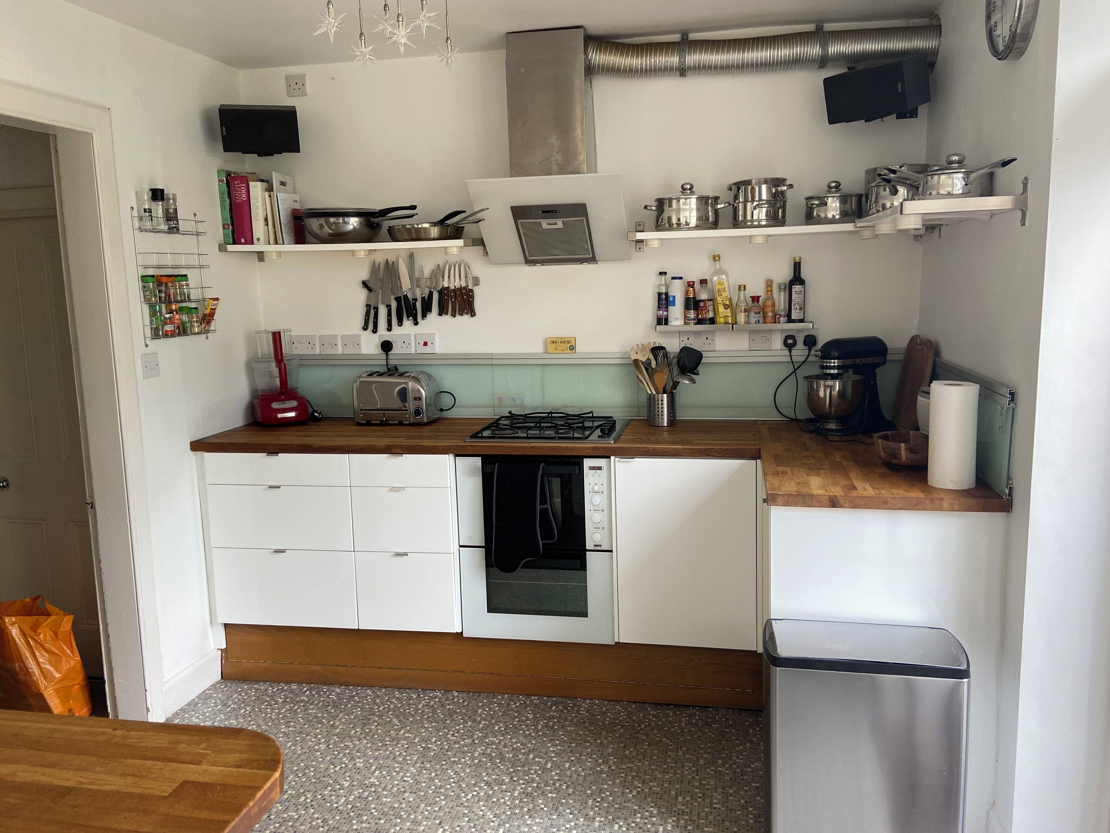 Cocina compacta con armarios blancos, estufa a gas, lavavajillas y diversos utensilios y electrodomésticos.