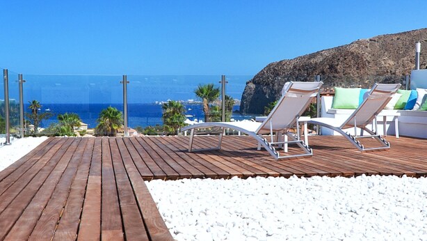 Een houten terras met lounge fauteuils en een rotsachtige klif op de achtergrond.