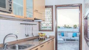 Een keuken met een spoelbak, fornuis en kasten, die uitkomt op een zitgedeelte buiten met uitzicht op de zee.