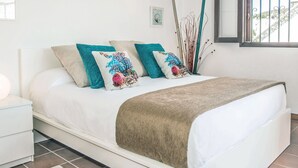 Een net opgemaakt bed met witte lakens en een bruin plaid, met twee decoratieve kussens met bloemmotieven.