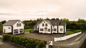 A row of three white houses with black trim, set in a rural area with a gravel driveway and lush greenery. - Forestside House - spacious house perfect for groups and families (Ballycastle)