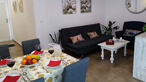 A living room with a black sofa, a dining table set with fruit and wine, and a white lamp. - Nice house with large solarium in Cordoba (Córdoba)