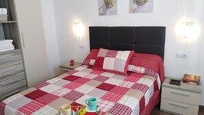 A neatly made bed with a red and white checkered bedspread, a small bedside table with a red lantern, and a wall-mounted light fixture. - Nice house with large solarium in Cordoba (Córdoba)
