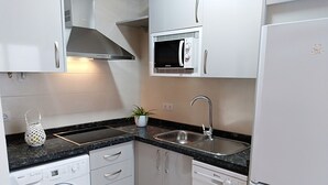 A compact kitchen with white cabinets, a built-in microwave, a stainless steel sink, a washing machine, and a dishwasher. - Nice house with large solarium in Cordoba (Córdoba)