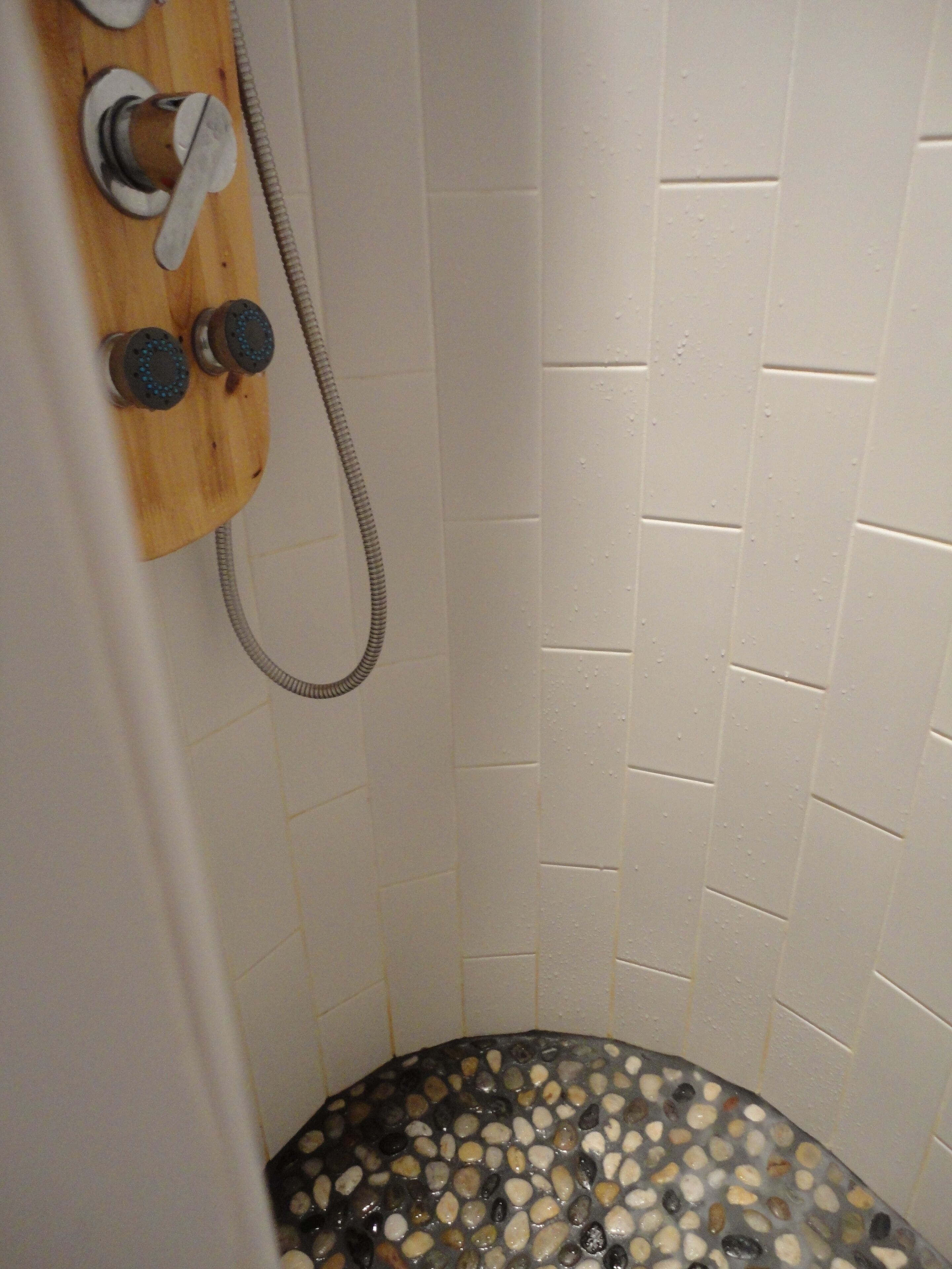 A shower area with a wooden shower panel, a hose, and a tiled wall.
