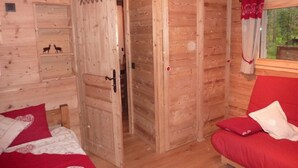 Quarto de cabana de madeira com cama, sofá vermelho e porta para outro cômodo.