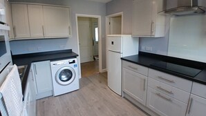 Cocina compacta con lavadora, refrigerador y armarios de colores claros.