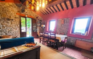 Habitació acollidora amb paret de pedra, un sofà blau, taula de dinar amb cadires i una finestra gran.