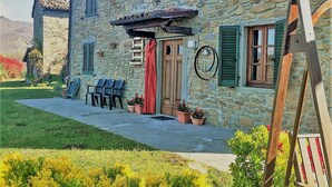 A stone building with a wooden door, green shutters, and a small porch with chairs. - Barga -cottage & barn 6 hctres of land, private pool, WIFI , stunning views! (Barga)