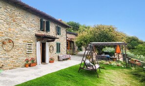 Una casa de pedra amb jardí, mobiliari exterior i un tobogan.