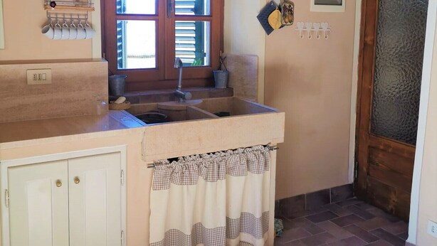A kitchen with a double sink, a window with blinds, a small shelf with kitchen utensils, and a door with a frosted glass panel. - Barga -cottage & barn 6 hctres of land, private pool, WIFI , stunning views! (Barga)