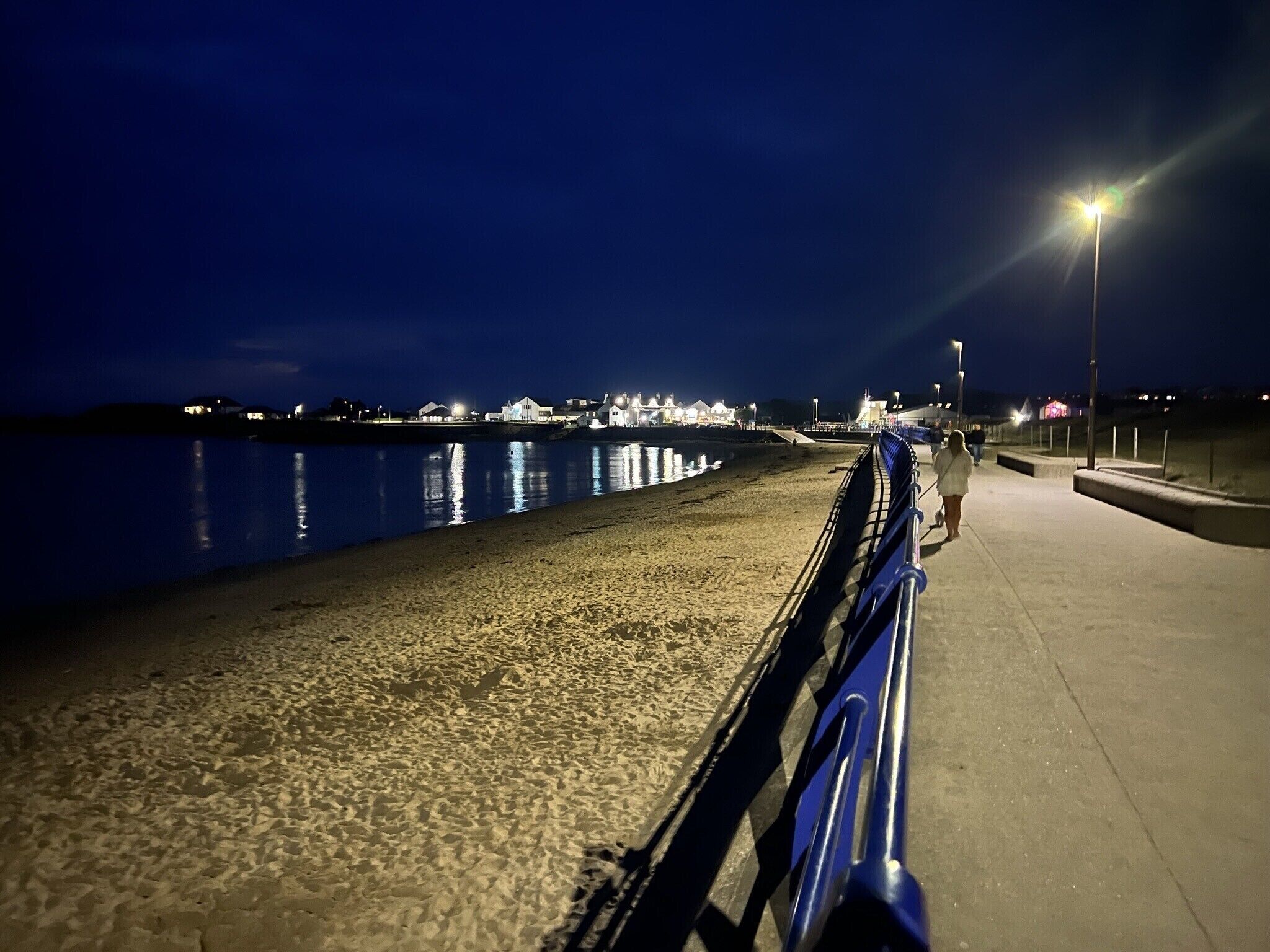 A nighttime beach scene with a paved walkway and a railing.