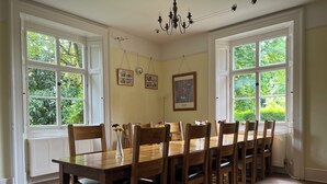 A dining room with a long wooden table and chairs, large windows with a view of greenery, and a chandelier. - 10-16 persons. Variable rates. 4 large (20-25 sq mtr) en suite rooms. (Colerne)