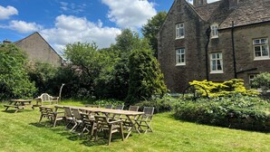 A traditional stone building with a pitched roof and chimneys, surrounded by lush greenery and a clear blue sky. - 10-16 persons. Variable rates. 4 large (20-25 sq mtr) en suite rooms. (Colerne)