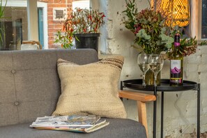 A cozy seating area with a grey sofa, a woven pillow, and a small table with a wine bottle and glasses.