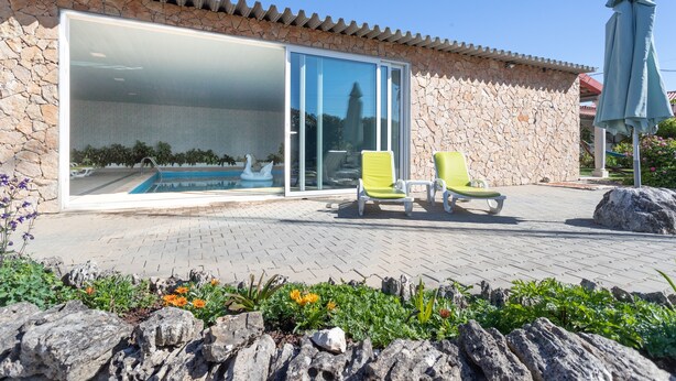 A poolside area with a stone wall, two lounge chairs, and a large sliding glass door leading to a pool.
