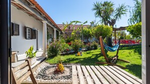 A patio with a wooden bench, a hammock, and a garden with various plants and flowers.