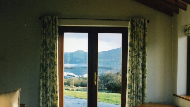 A room with a bed, a wicker sofa, and a view through a large sliding door to a scenic outdoor area.