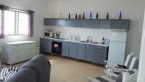 A compact kitchen with a microwave, coffee maker, and a refrigerator. There is a sofa and a chair in the living area.