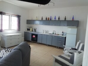 A compact kitchen with a microwave, coffee maker, and a refrigerator. There is a sofa and a chair in the living area.