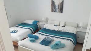 A hotel room with two beds, each with blue and white bedding, white headboards, and bedside tables with lamps.